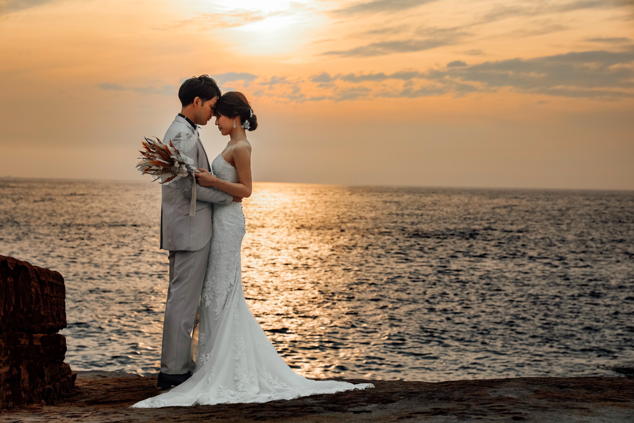 夕陽の海辺で寄り添う新郎新婦